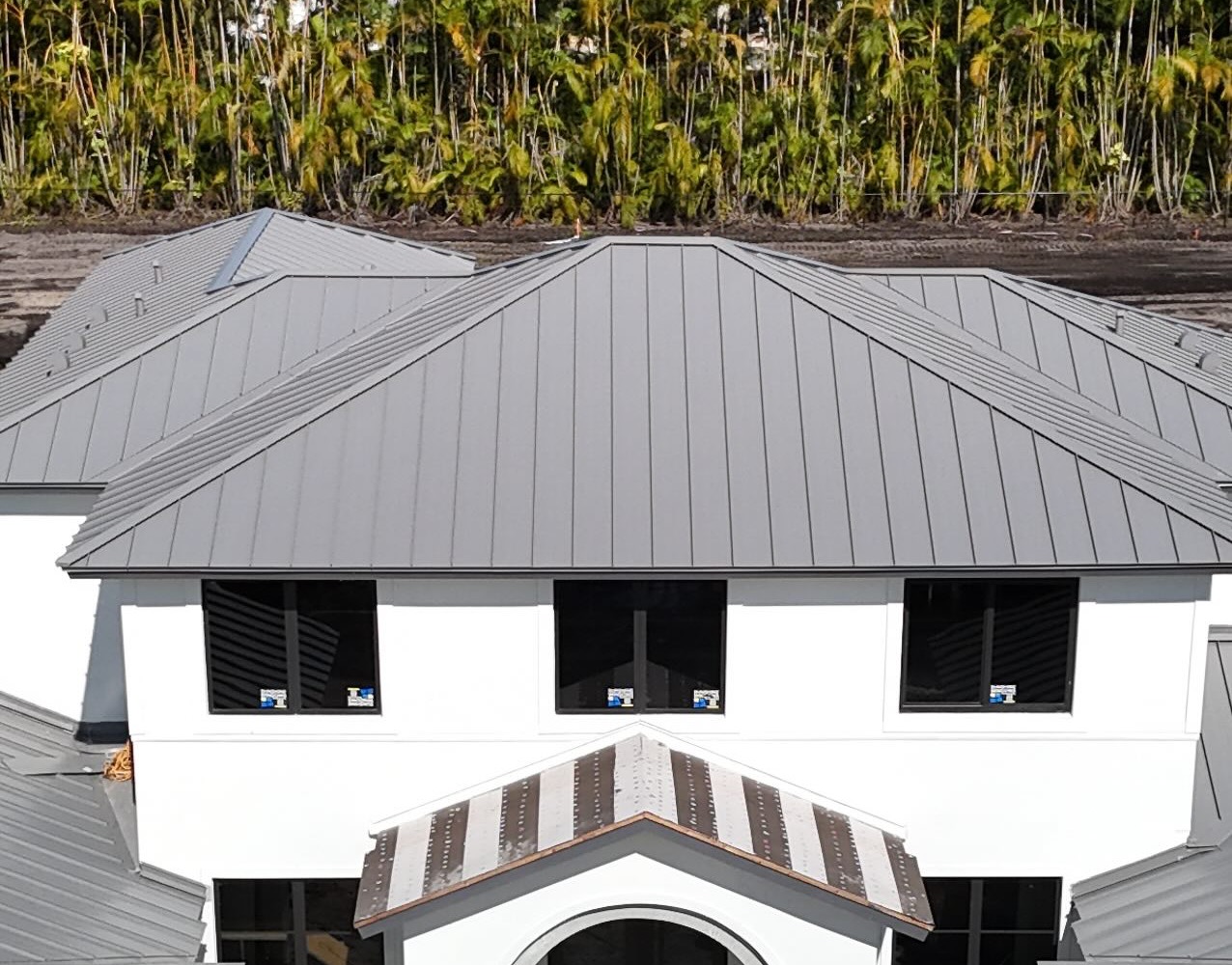 Slate-grey standing-seam metal roof on a white Mediterranean home under construction