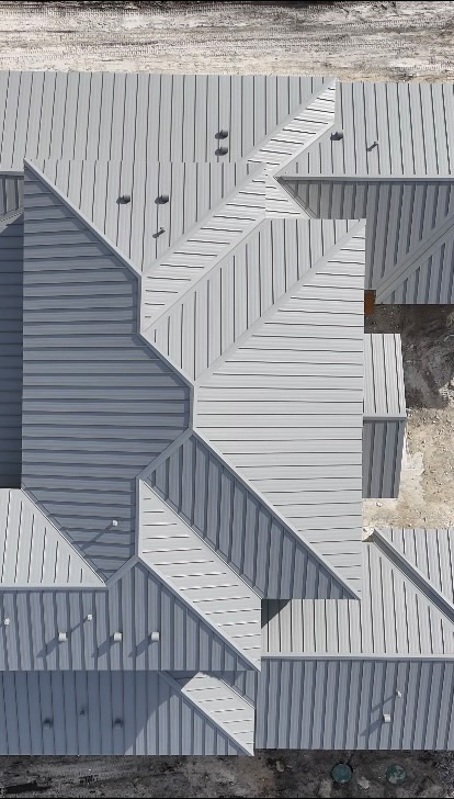 Overhead drone view of a grey standing-seam metal roof with many hips and valleys